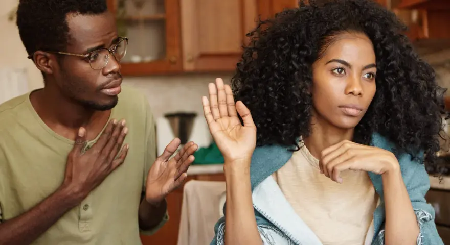 Un homme avec des lunettes parle avec passion, la main sur le cœur, tandis que sa femme, le regard ailleurs, lève une main en signe d'arrêt. Il dit : "je ne supporte plus ma femme.