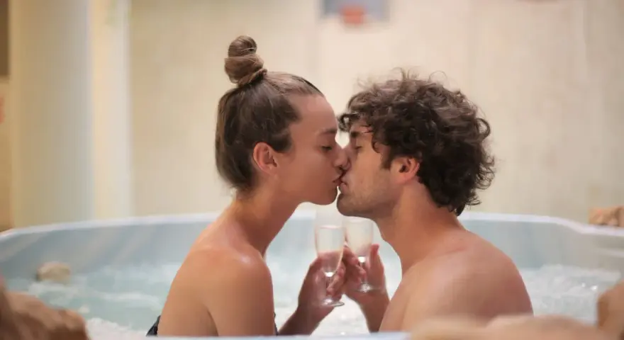 Un couple s'embrasse tendrement dans un jacuzzi, deux coupes de champagne à la main, pour un bain romantique inoubliable.