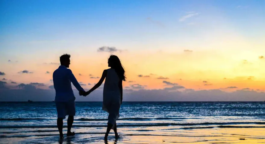 Silhouettes d'un couple se tenant la main sur une plage au coucher du soleil. Il tient à moi mais n'est pas amoureux, juste un ami.
