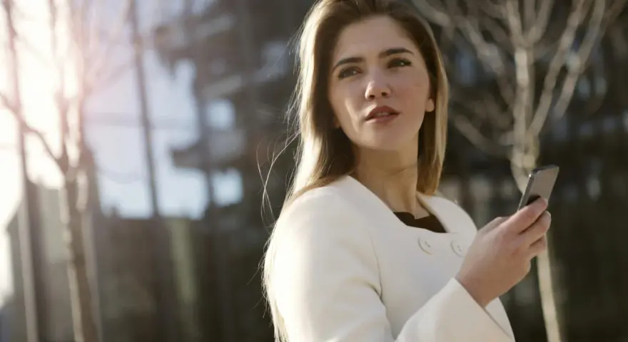 Une femme en manteau blanc tient un téléphone, prête à challenger un homme par sms.