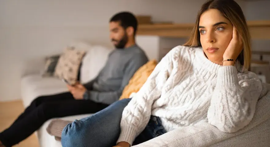 Un couple s'ennuie dans son couple, chacun absorbé par son téléphone sur le canapé, le regard perdu dans le vide.