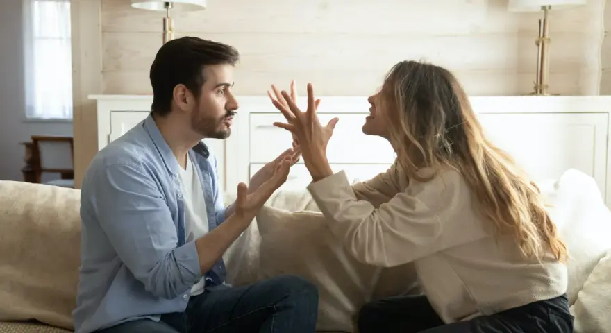 Un couple se dispute sur un canapé. L'homme semble frustré, peut-être parce qu'il est jaloux.