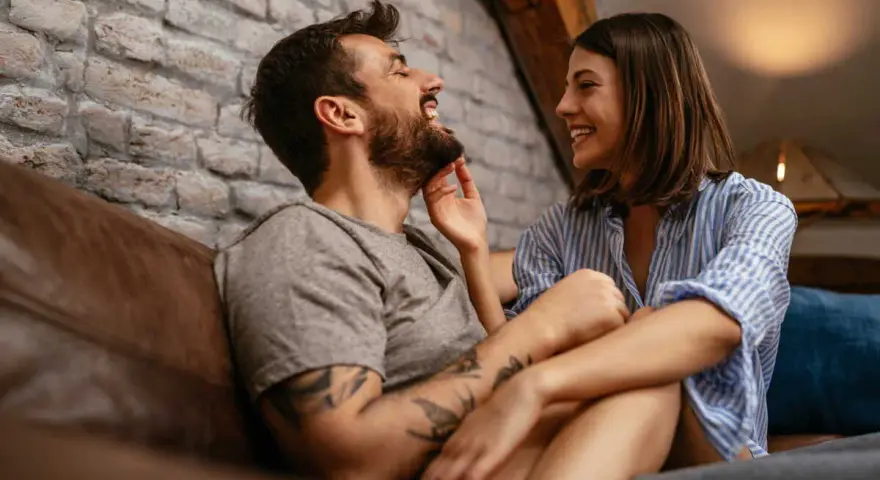 Un couple rit et se regarde tendrement sur un canapé. Le vrai amour, c'est cette complicité.