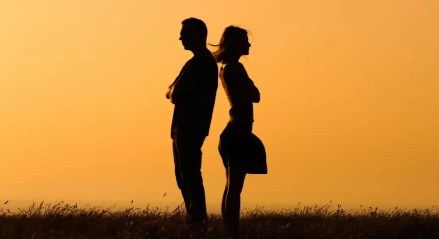 Silhouettes d'un homme et d'une femme dos à dos, bras croisés, symbolisant la communication paradoxale dans un paysage au coucher du soleil.