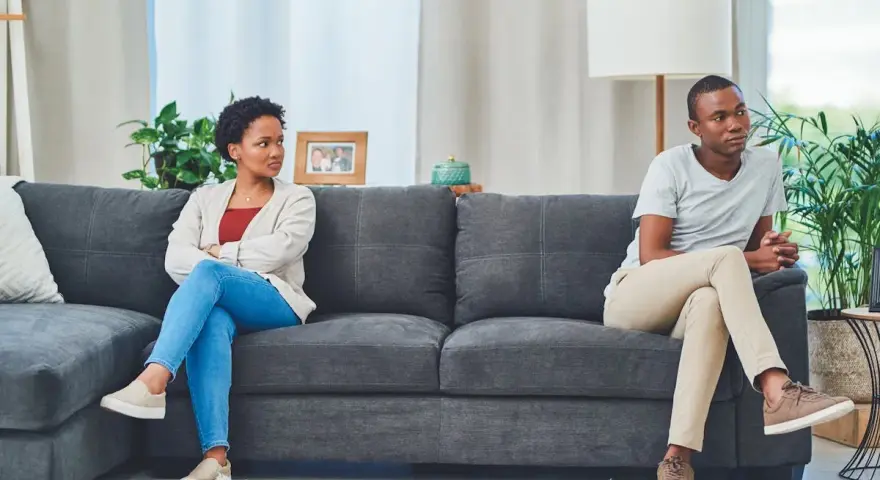 Un couple assis sur un canapé, dos à dos, l'air distant. Elle, les bras croisés, le regarde avec une expression de lassitude. Il, pensif, détourne le regard. Je l'aime mais je ne le supporte plus.