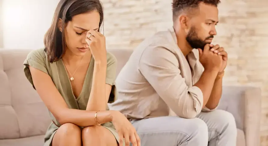 Un couple assis dos à dos, visiblement affecté par des disputes incessantes. La femme se tient la tête, l'air accablé, tandis que l'homme fixe le vide, les mains jointes.