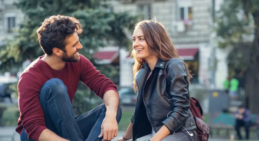 Un couple rit en s'asseyant dehors. Un moment complice pour montrer à son partenaire qu'on a envie de lui.