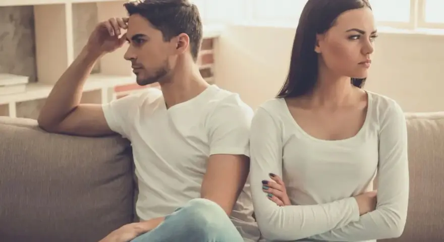 Un couple assis sur un canapé, dos à dos, visiblement en conflit. Elle croise les bras, l'air contrarié, comme s'il la prenait pour acquise.