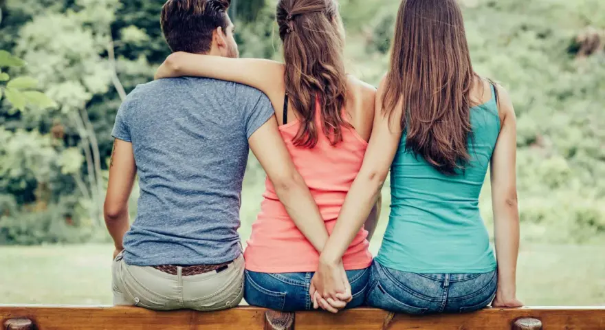 Trois personnes assises sur un banc, un homme entre deux femmes. Les mains des femmes se serrent derrière le dos de l'homme. Je ne le trouve pas beau mais il m'attire.