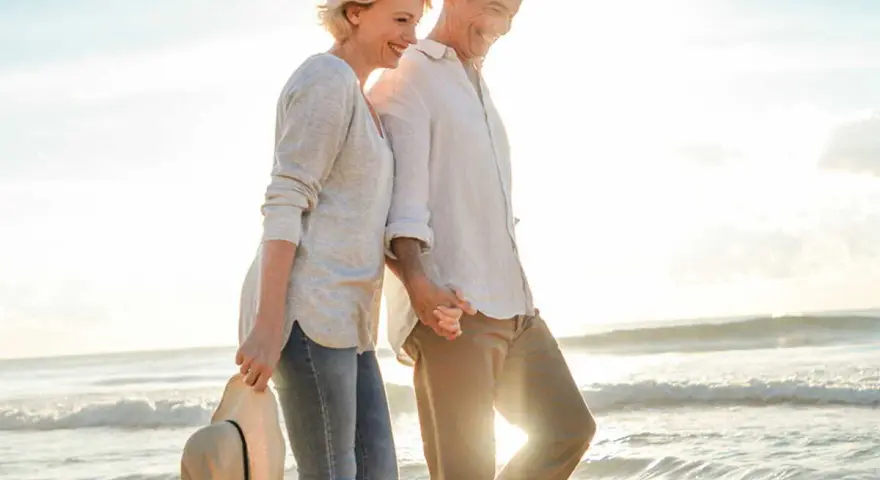 Un couple profite d'un rendez-vous amoureux sur la plage, main dans la main, au coucher du soleil.