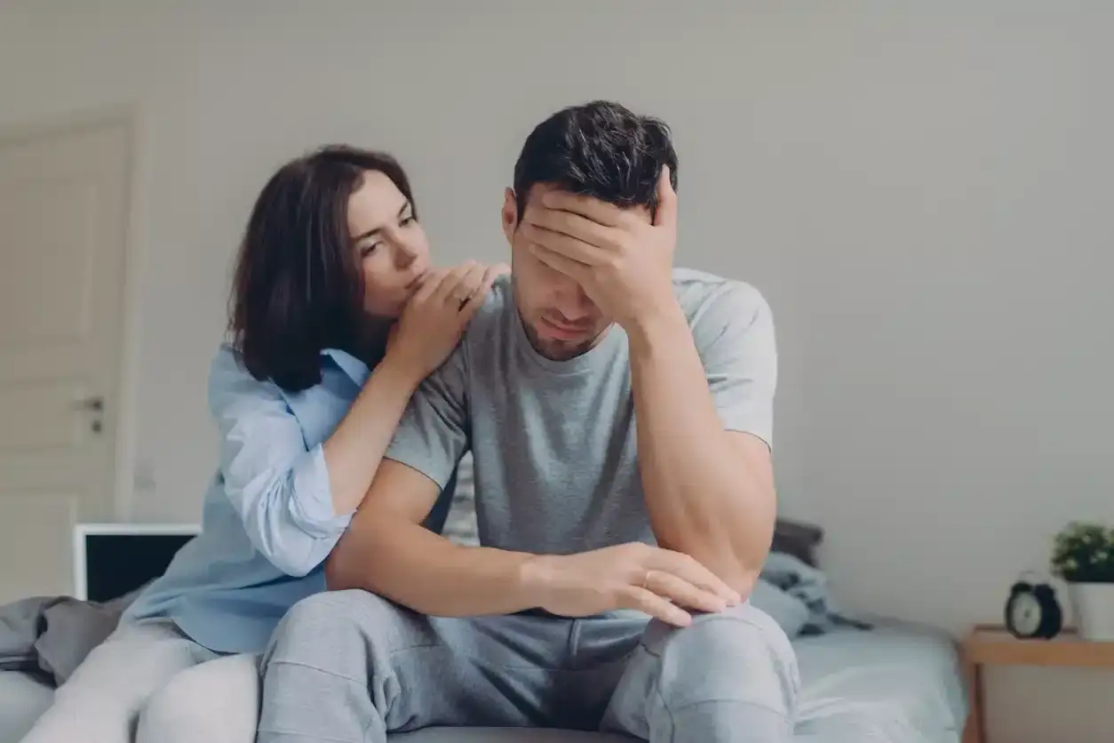 Une femme réconforte son mari, qui semble accablé. Elle pose une main sur son épaule, mais mon mari n'est pas affectueux, alors elle se sent seule.