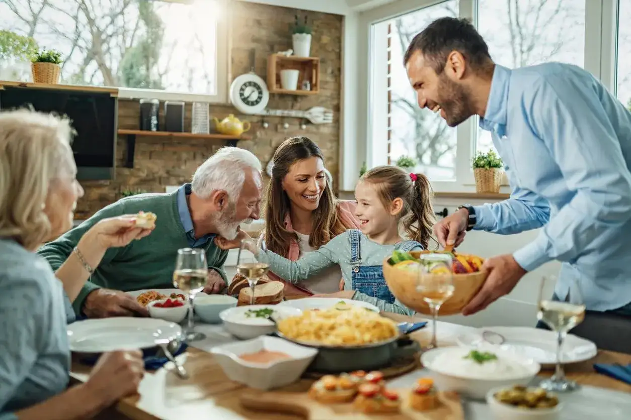 Un p&egrave;re joyeux sert un plat de fruits et l&eacute;gumes &agrave; sa famille r&eacute;unie autour d'une table. Il parle de moi &agrave; son entourage, cr&eacute;ant une atmosph&egrave;re chaleureuse.