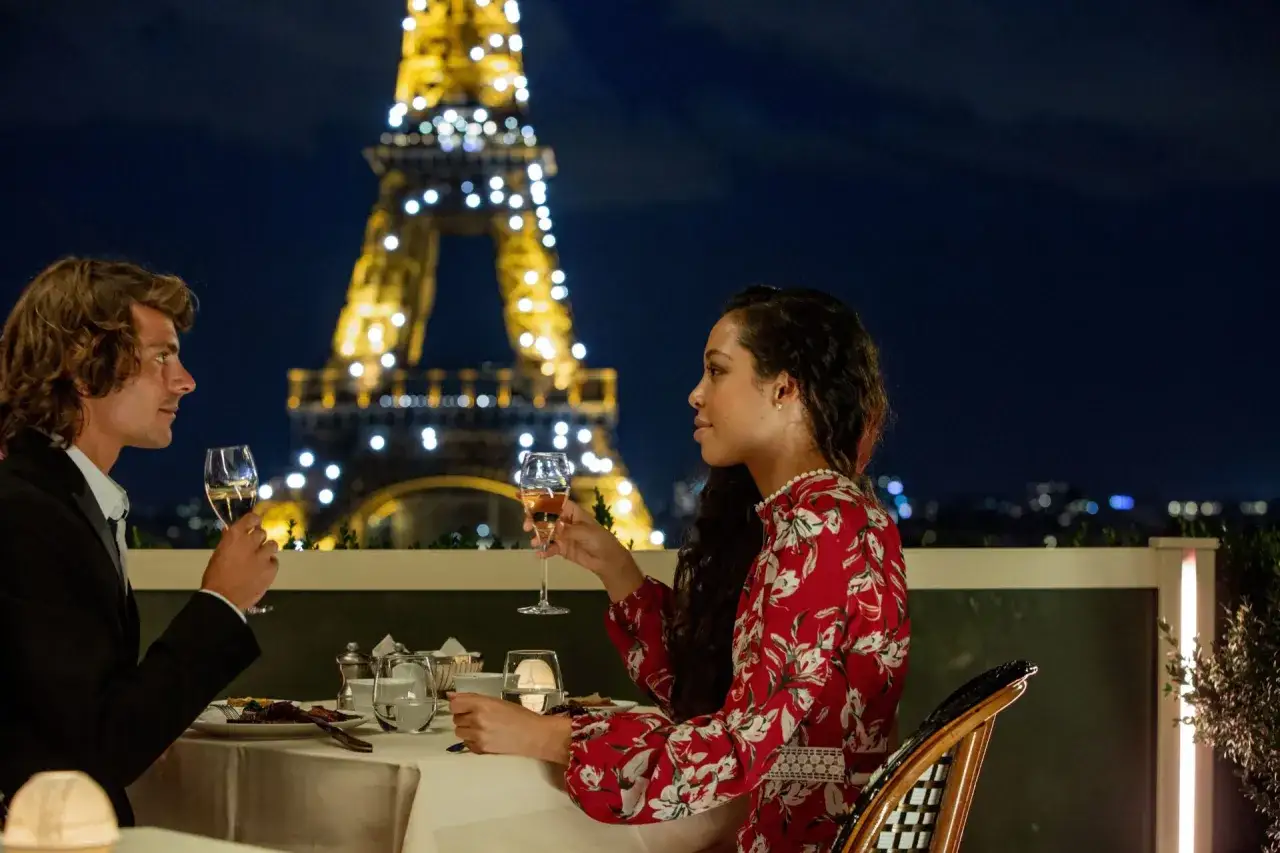 Un couple partage un dîner romantique à Paris, avec la Tour Eiffel illuminée en arrière-plan. Un rendez-vous amoureux parfait.