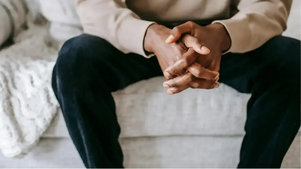 Homme assis, mains jointes, pensif. Il pourrait réfléchir à un besoin sexuel homme, ou à tout autre désir profond.