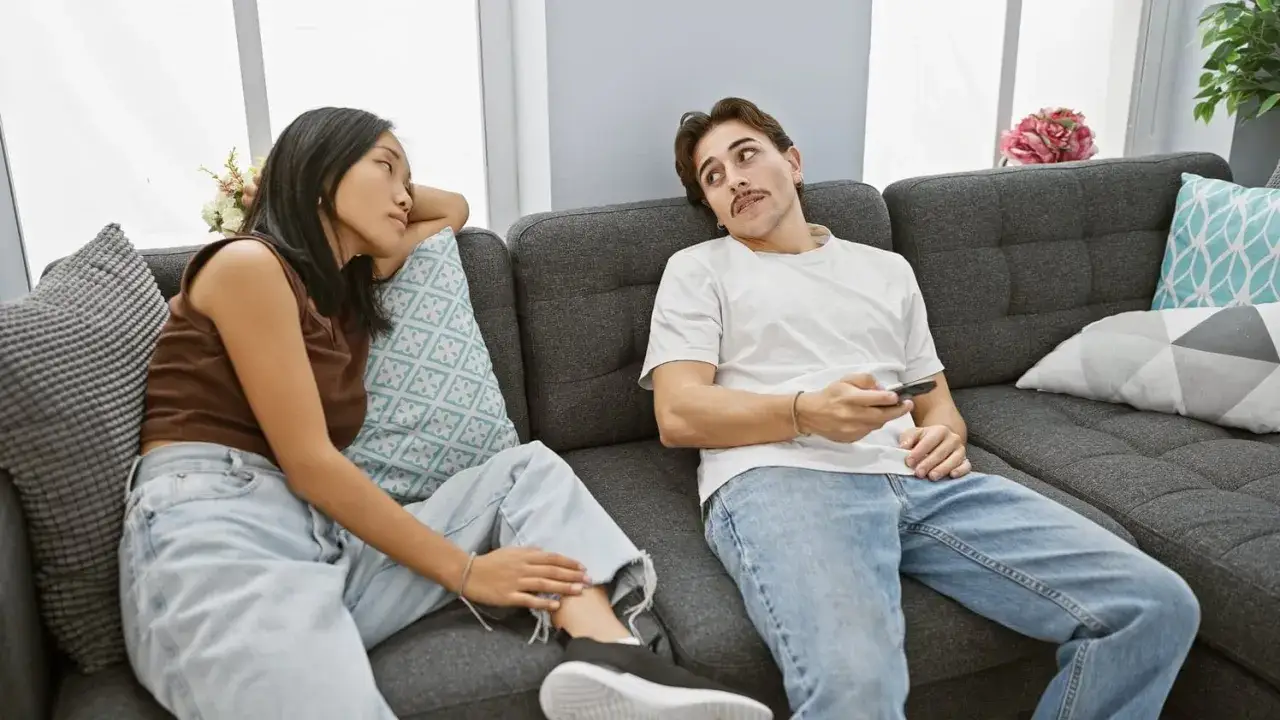 Un couple sur un canapé. Elle le regarde, pensant :