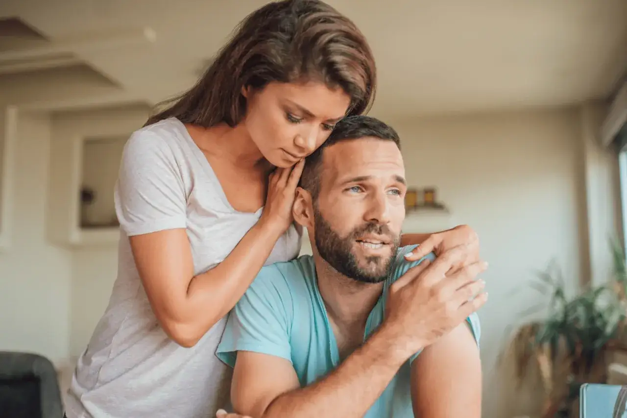 Une femme r&eacute;conforte son conjoint, le bras autour de son &eacute;paule. Elle semble pr&eacute;occup&eacute;e, peut-&ecirc;tre se demande-t-elle que faire quand on a des doutes sur son conjoint.