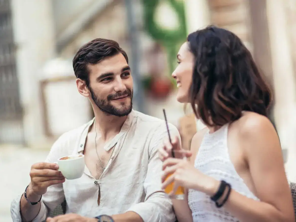 Un homme et une femme souriants partagent un café, il semble vouloir se faire désirer.