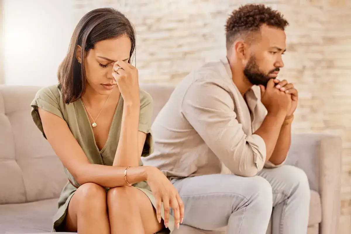 Un couple qui se dispute, visiblement malheureux, assis dos à dos sur un canapé, le regard perdu dans le vide.