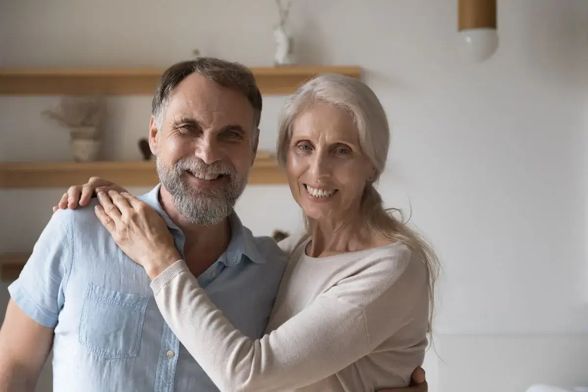 Un couple souriant, lui a 45 ans, sa femme pose sa main sur son épaule. Leur libido est intacte.