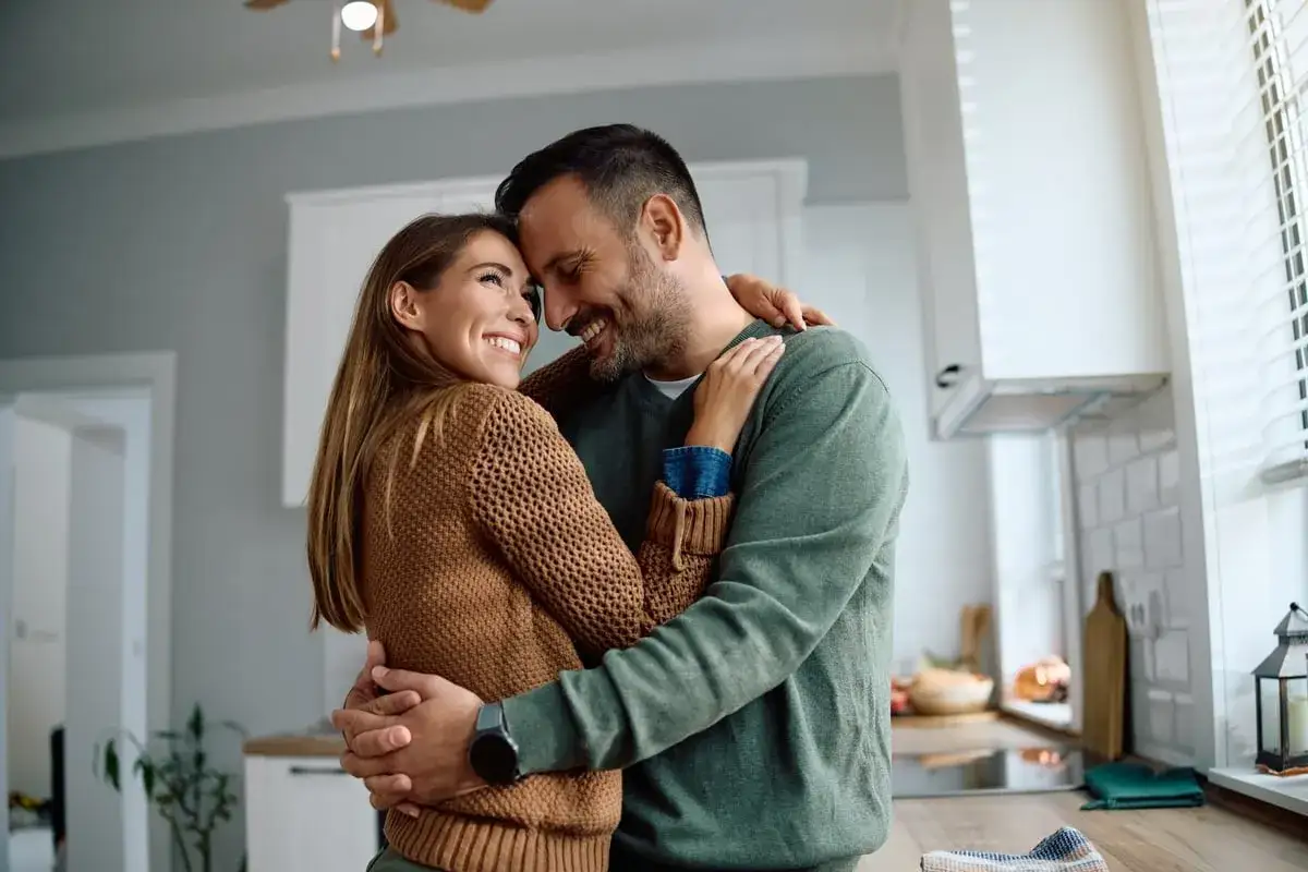 Un couple s'enlacet dans une cuisine, leurs fronts se touchant. Un moment tendre qui montre comment dire je t'aime sans le dire.
