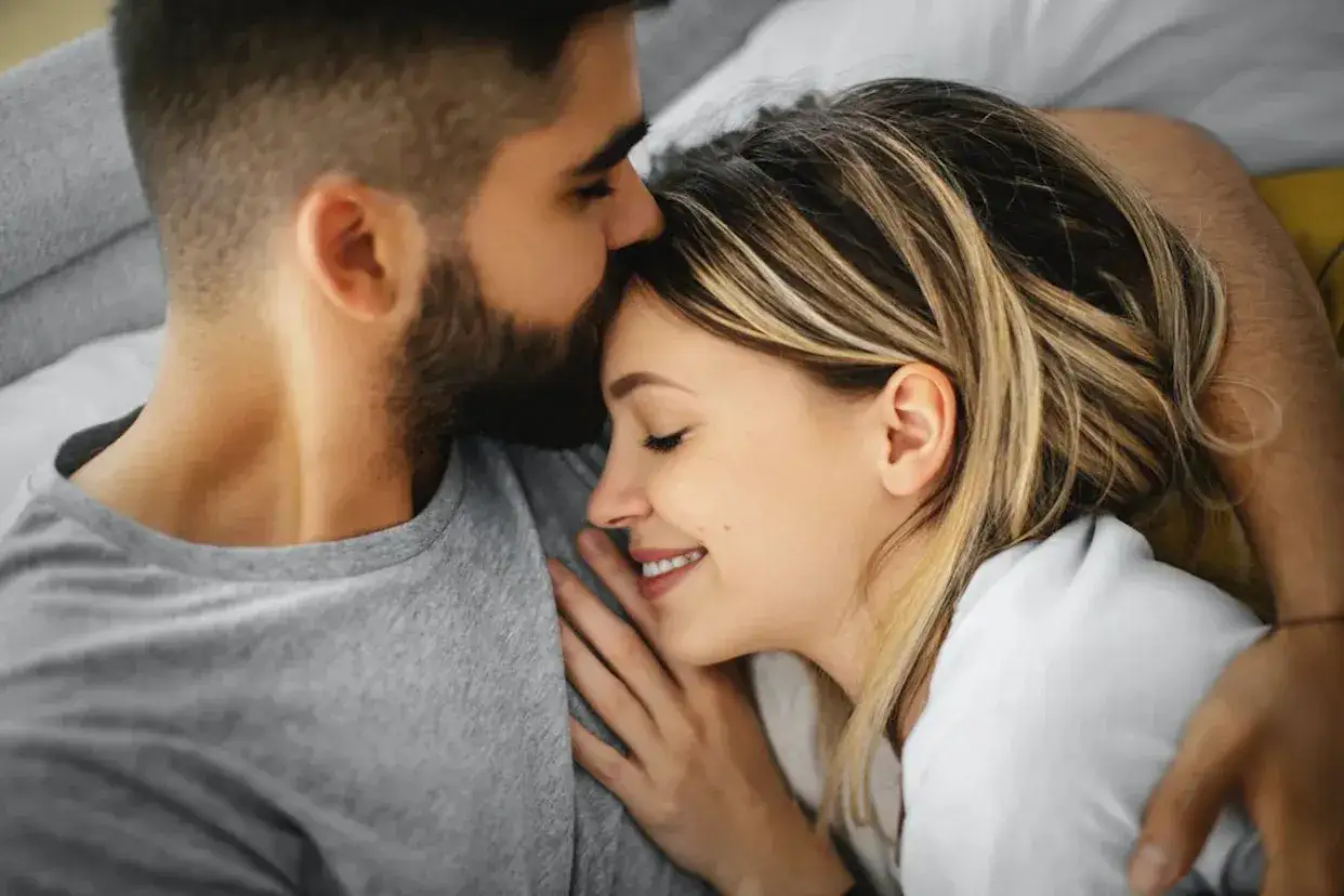 Un homme embrasse le front d'une femme endormie, un moment de tendresse et de c&acirc;lin amoureux.