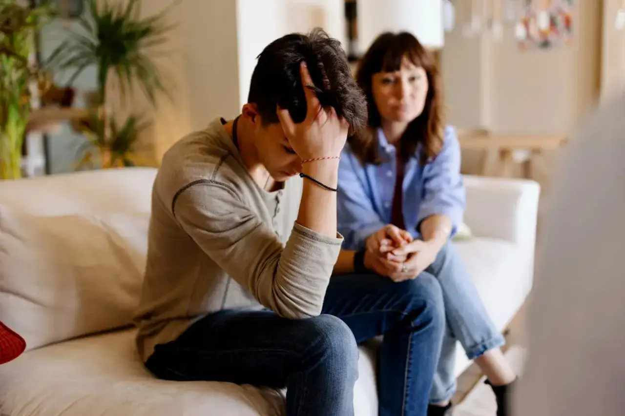 Un adolescent se sent d&eacute;laiss&eacute; par son conjoint, la t&ecirc;te dans les mains, tandis que sa m&egrave;re le regarde avec inqui&eacute;tude.