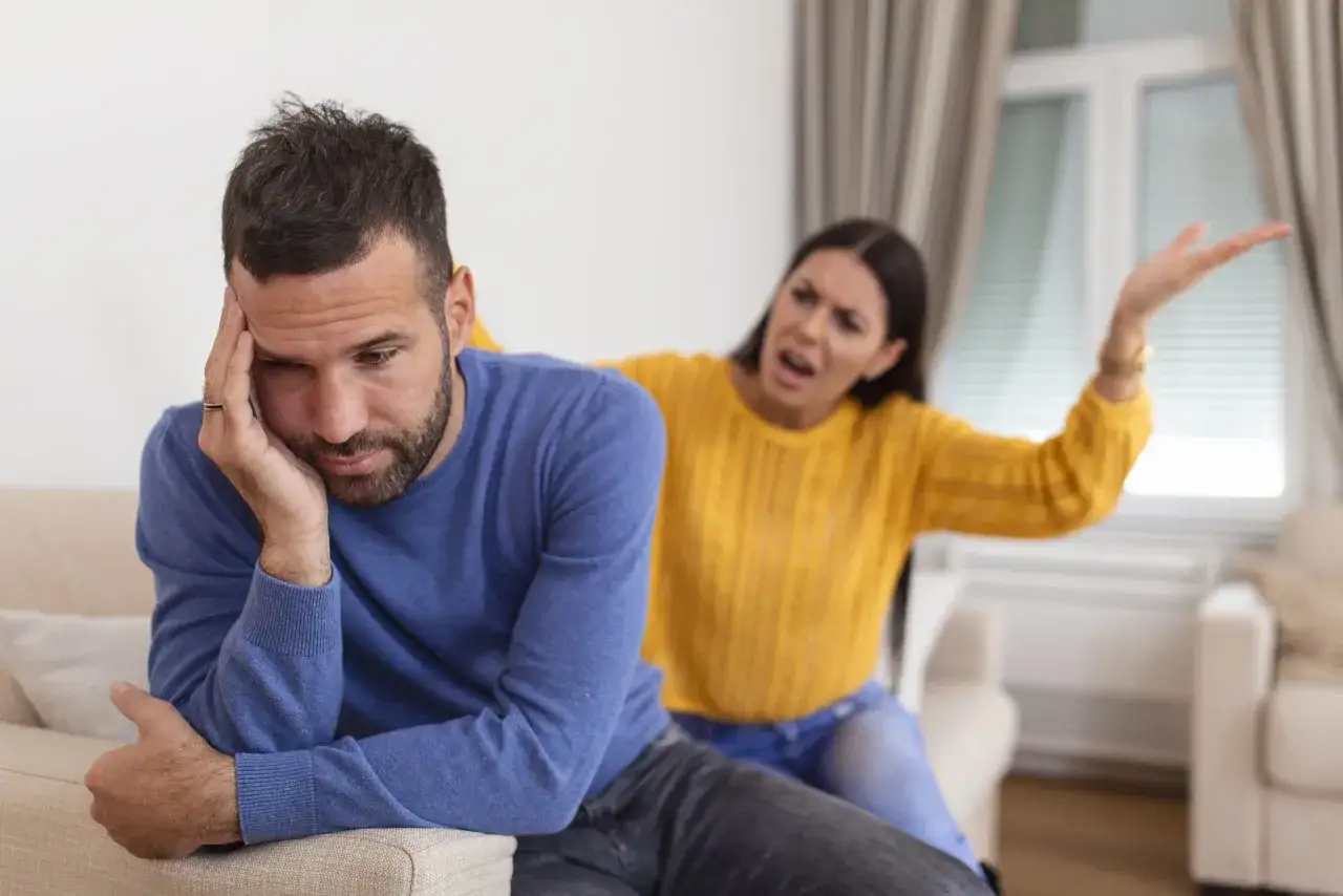 Un homme fatigué se tient la tête, tandis qu'une femme en colère lui crie dessus. Une scène typique de la crise des 1 an d'un couple.