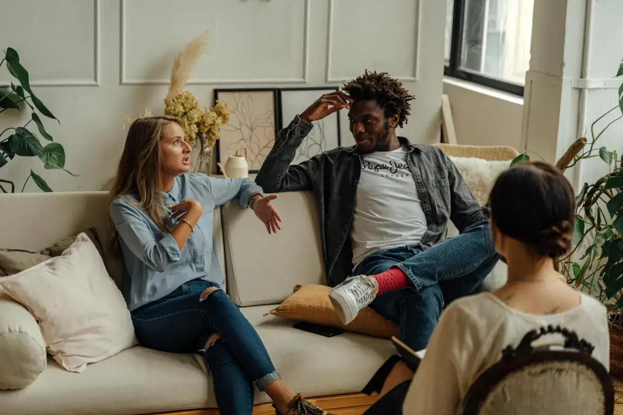 Un couple discute avec un th&eacute;rapeute pour calmer sa jalousie. La femme parle avec animation, l'homme &eacute;coute attentivement.