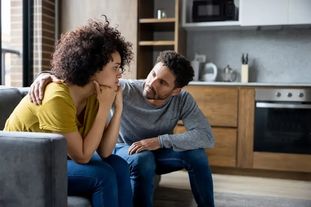 Un homme réconforte sa compagne après une dispute. Il lui pose la main sur l'épaule, un geste qui montre comment se comporter avec son homme après une dispute : avec douceur et compréhension.