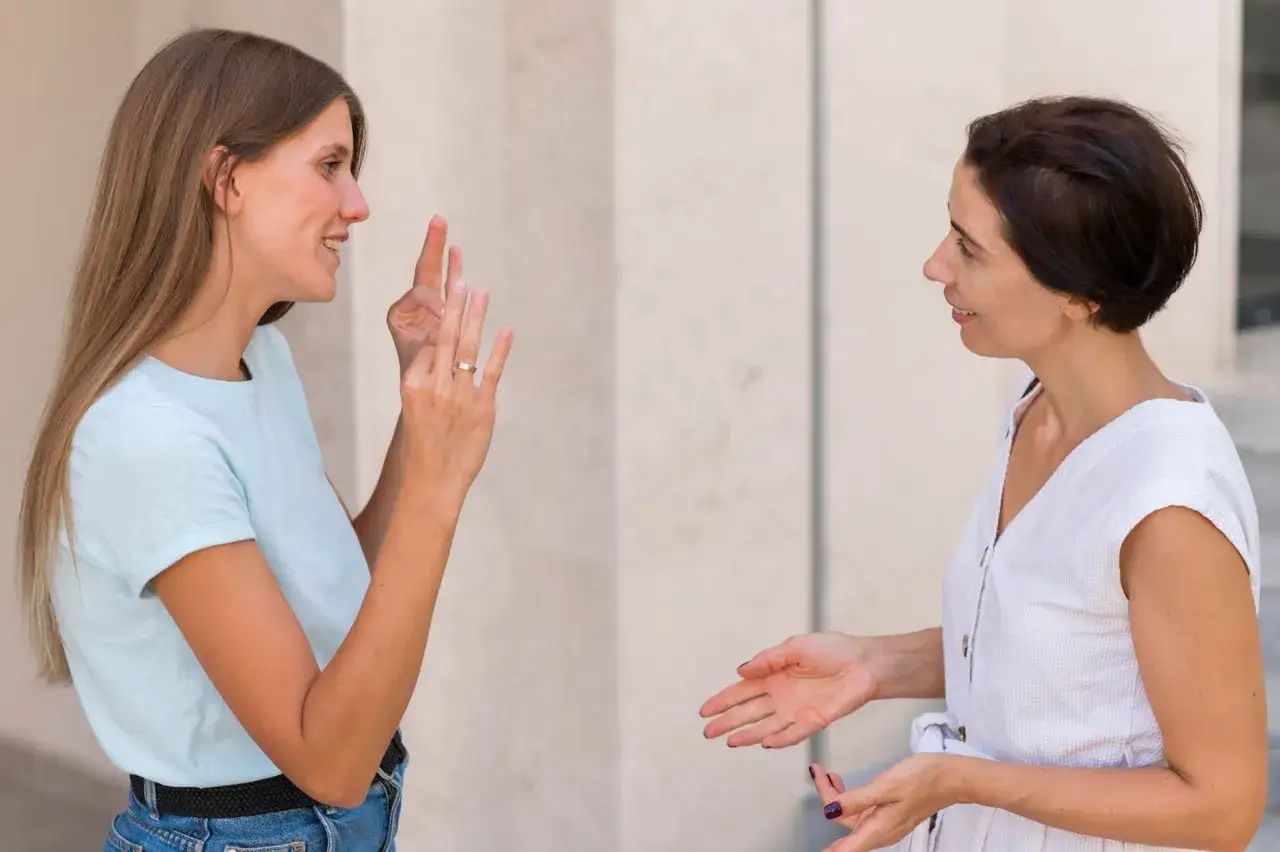 Deux femmes échangent des signes, un paradoxe de communication où les mains parlent plus fort que les mots.