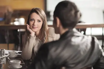 Une femme au regard fuyant psychologie, assise à une table de café, semble réfléchir à une conversation.