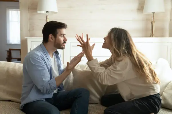 Un couple se dispute sur un canapé. L'homme semble frustré, peut-être parce qu'il est jaloux.