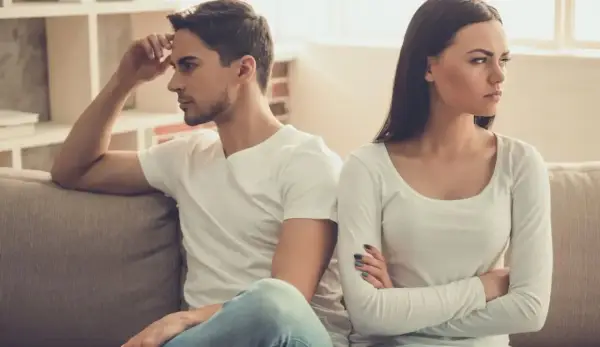 Un couple assis sur un canapé, dos à dos, visiblement en conflit. Elle croise les bras, l'air contrarié, comme s'il la prenait pour acquise.