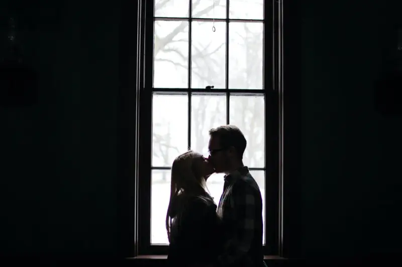 Silhouette d'un couple s'embrassant devant une fenêtre, une alchimie entre deux personnes capturée dans la lumière douce.
