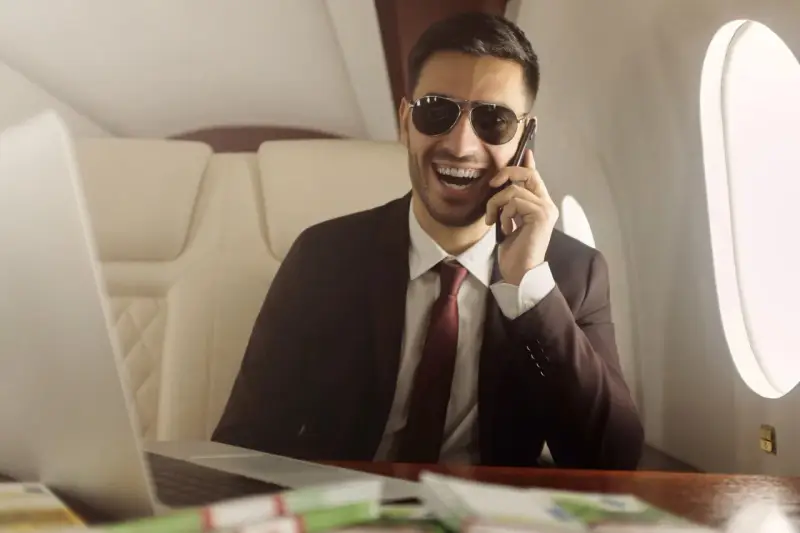 Un homme d'affaires souriant, lunettes de soleil, au téléphone dans un jet privé. Il semble rencontrer un homme riche pour conclure un accord.