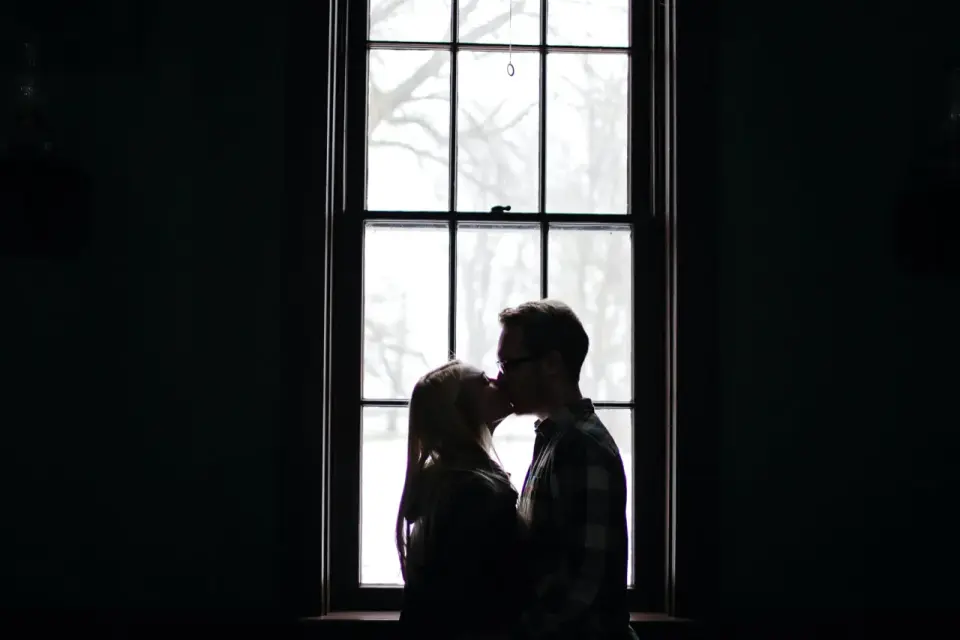 Silhouette d'un couple s'embrassant devant une fenêtre, une alchimie entre deux personnes capturée dans la lumière douce.